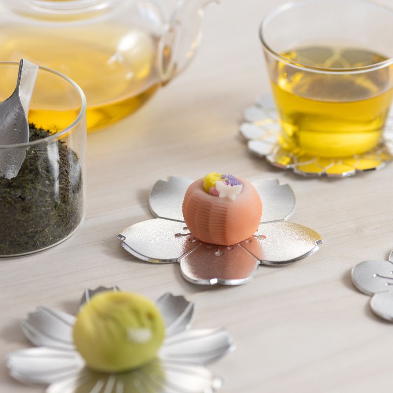 Tea set with a teapot, glass of tea, and decorative tea coasters on a light surface.