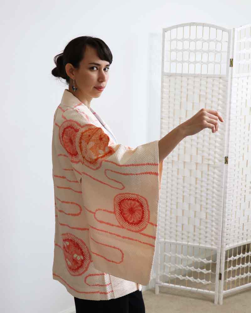 A woman wearing a  baby pink kimono, facing side front.