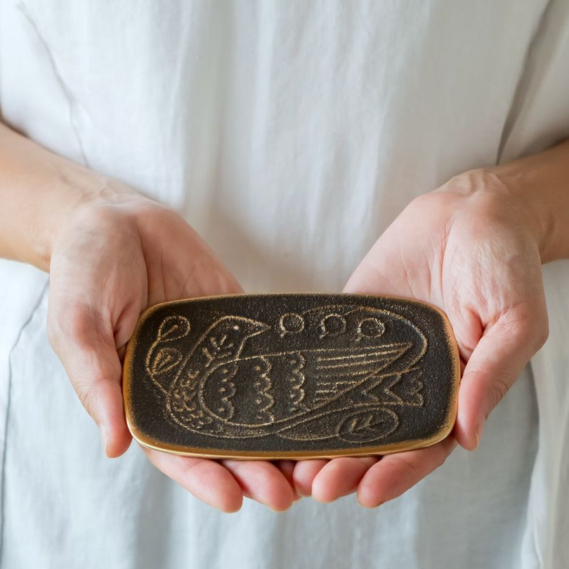 Person holding a decorative wooden object with intricate carvings against a neutral background