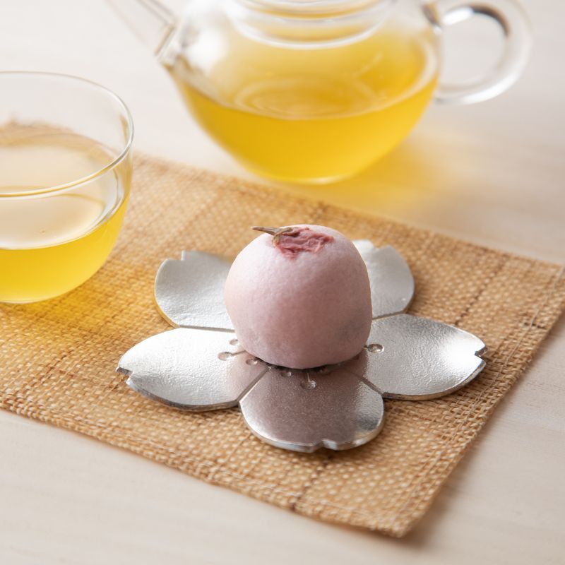 Pink dessert on a silver flower-shaped stand with two cups of tea in the background.