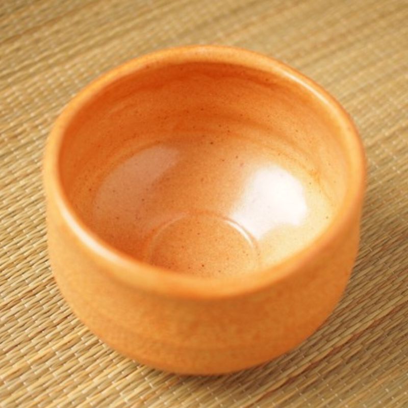 Akashino Matcha Tea Bowl from Nara Tea Co. with a slightly rough texture and an elegant orange color, seen from the side diagonally above the front.