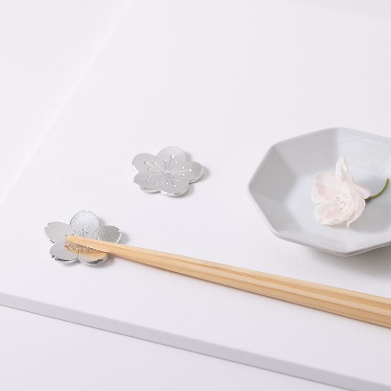 Silver flower-shaped chopstick rest with wooden chopsticks on a white surface.