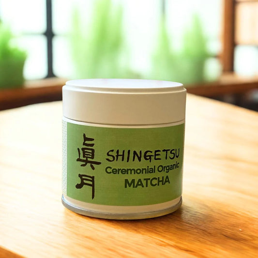 Container of Shingetsu Ceremonial Organic Matcha on a wooden table with a blurred green plant background