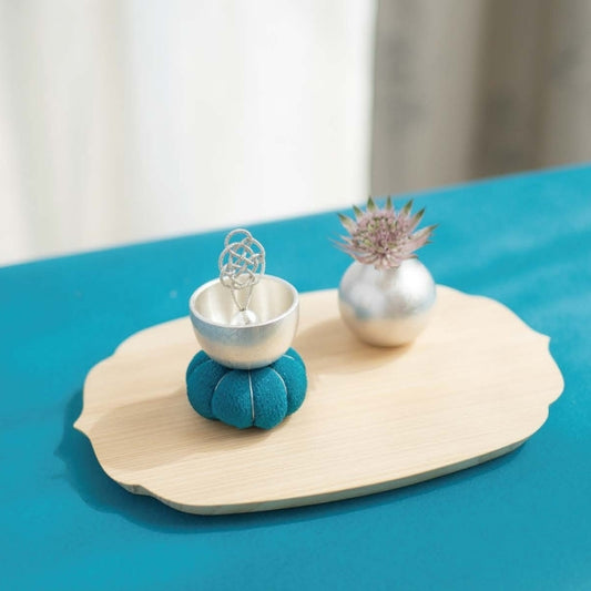 Decorative items including a blue teacup, silver bowl, and small plant on a wooden tray with a blue background.