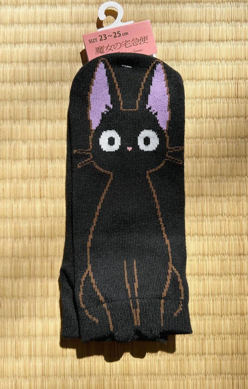Black cat-themed sock with purple ears on a beige mat