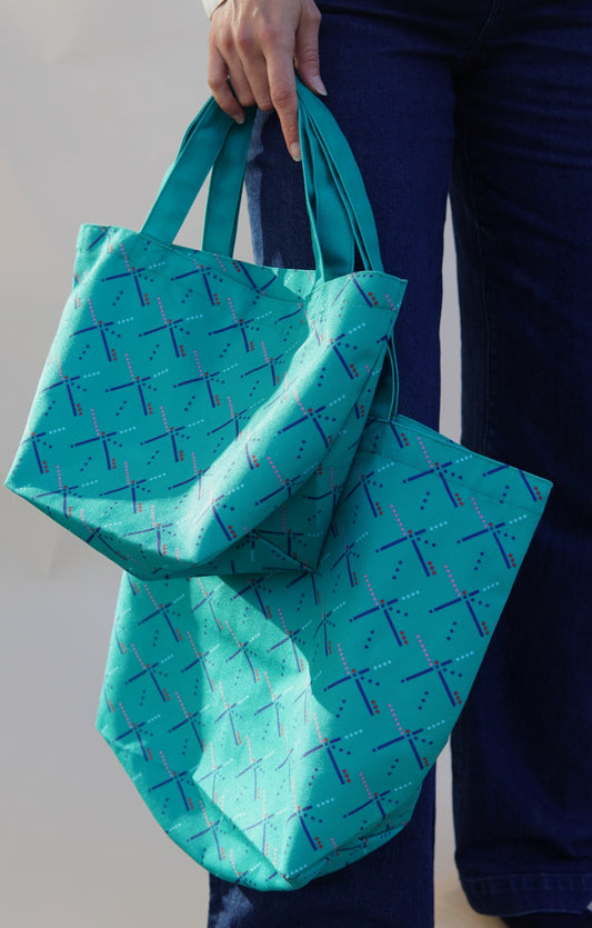 Person holding a teal reusable bag with a pattern against a neutral background