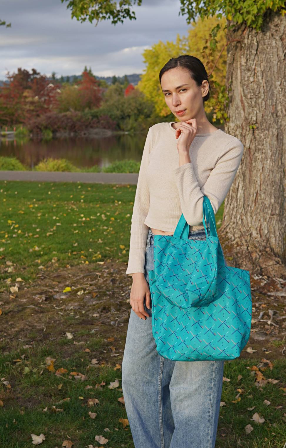 Woman holding a blue woven handbag in an outdoor setting with trees and grass.