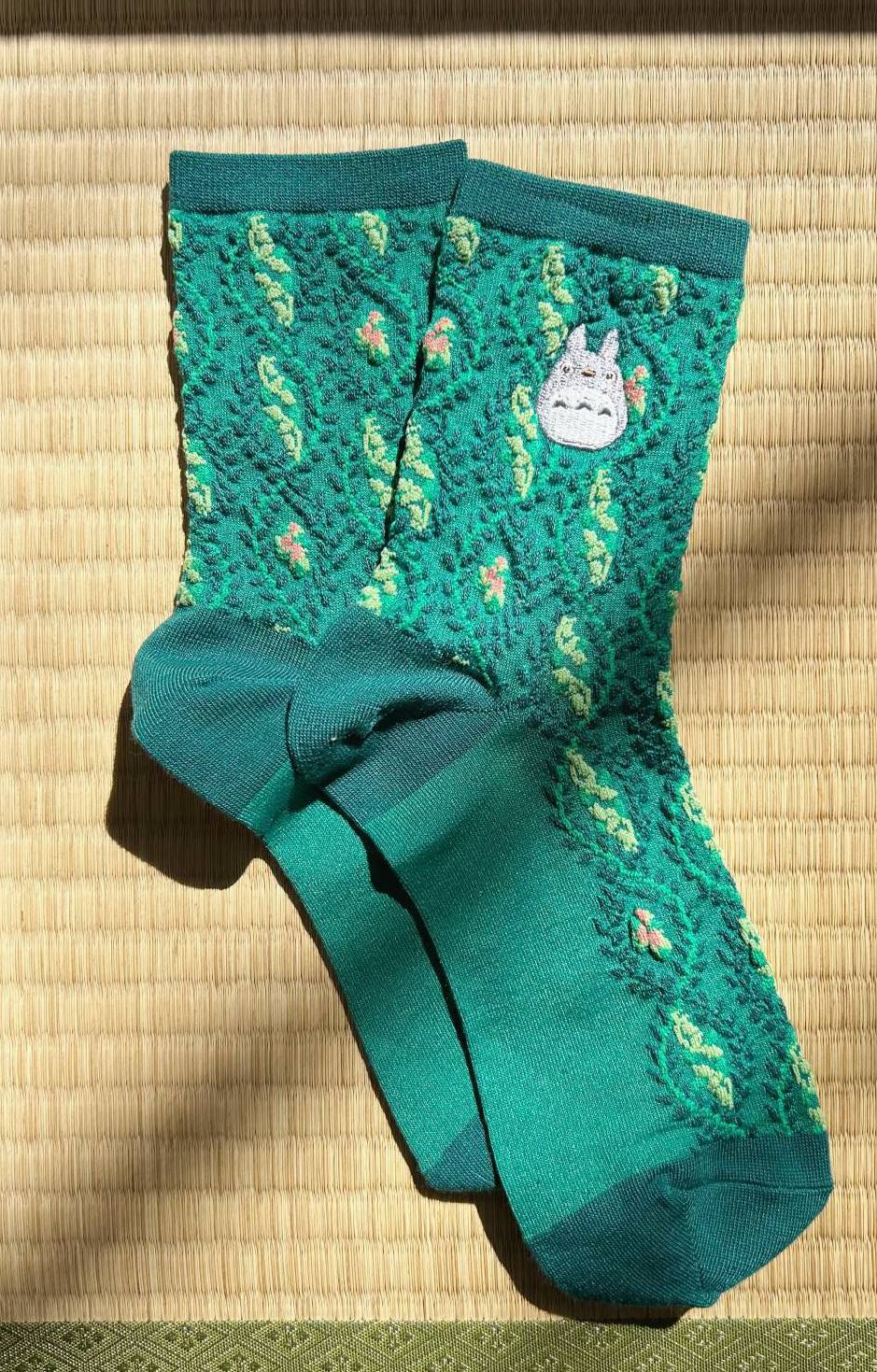 Teal socks with a totoro cartoon character on a woven mat