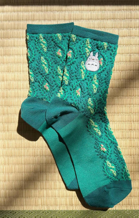 Teal socks with a totoro cartoon character on a woven mat